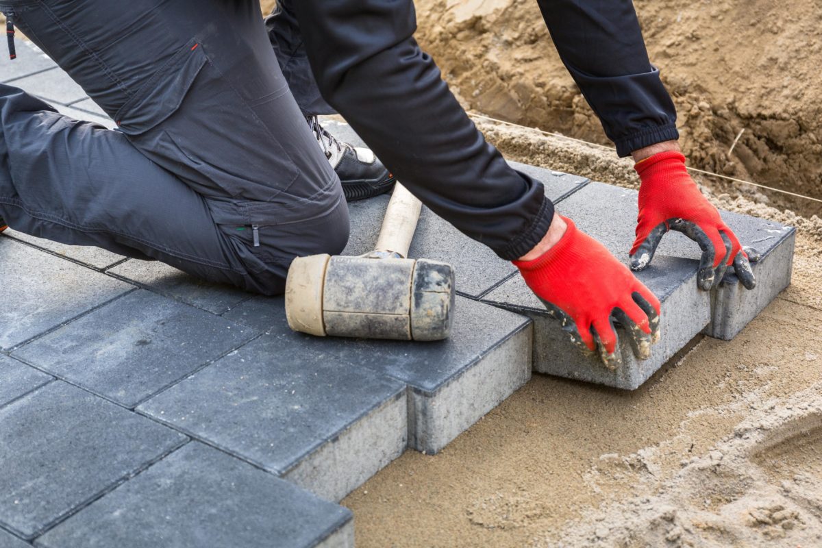 Services hands of worker installing concrete paver blocks with rubber hammer